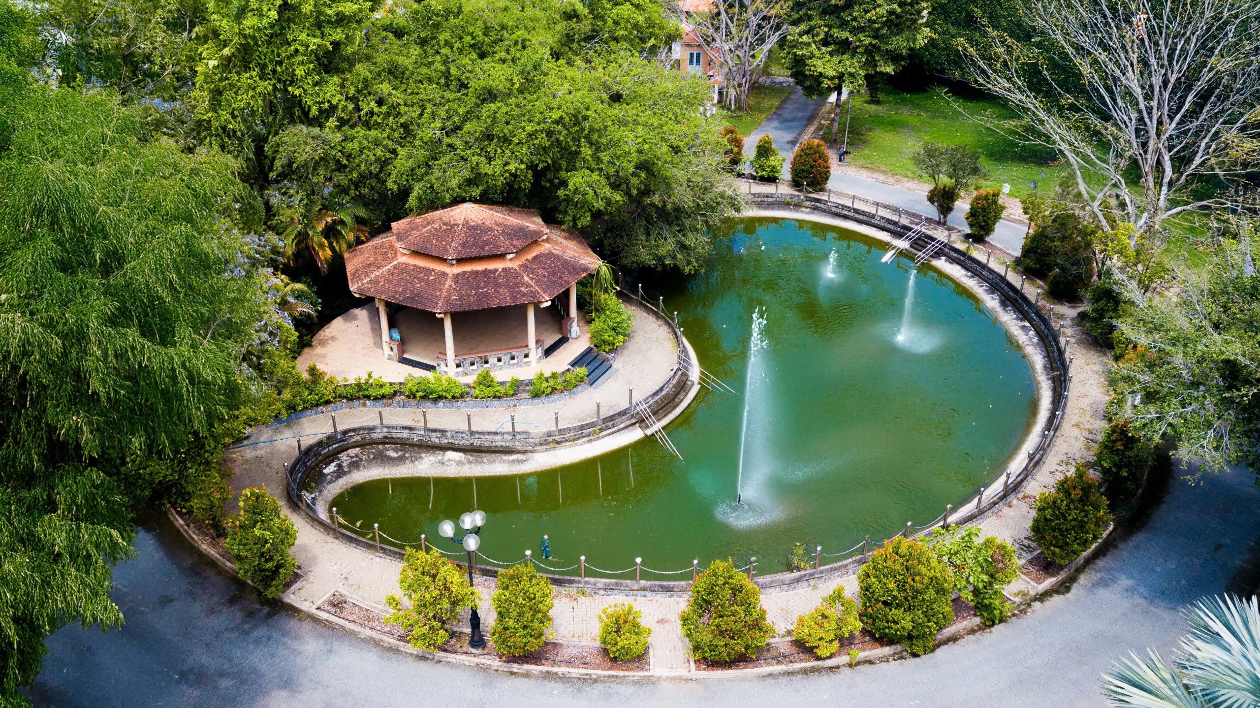 wide shot of a serene garden landscape with a modern minimalist pavillion and a quiet lake under a clear blue sky